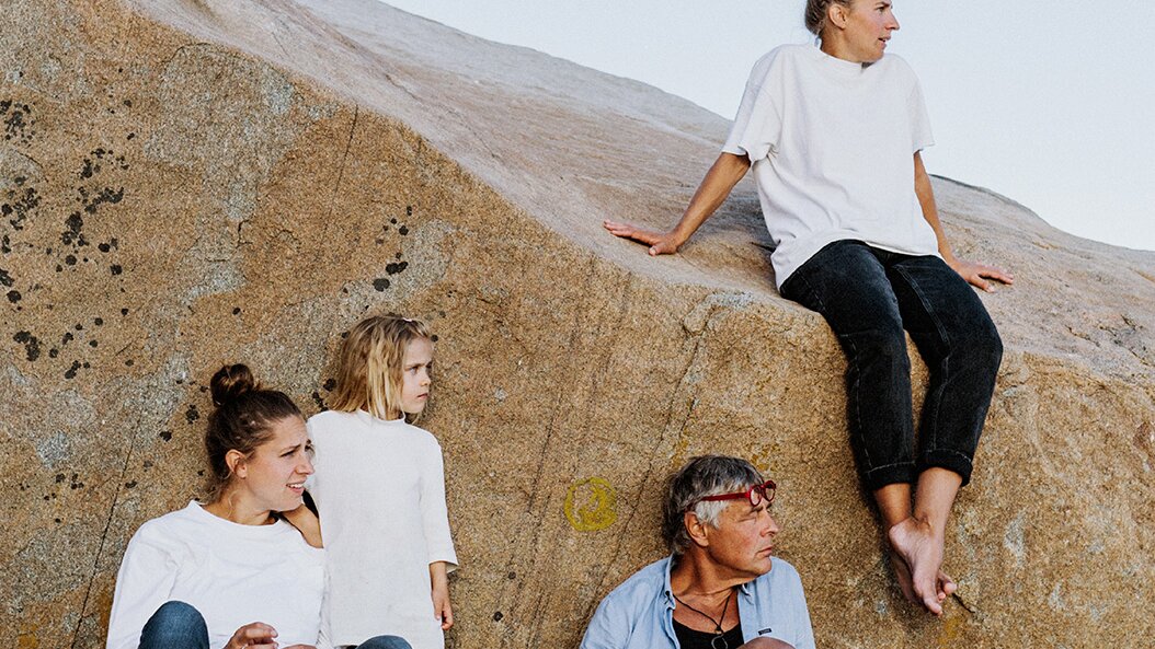En familj sitter ute på ett klippblock på sommaren och tittar på utsikten. Det är en familj på fyra som är klädda i jeans och ljusfärgade tröjor.